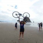 Amanda Koch holding her bike abover her head on a beach