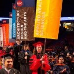 Representatives from each college walking holding college banner