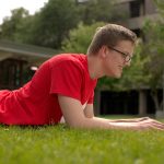 male student lying in the grass with laptop(Photo: Callie Lipki