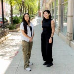 Two female students stand next to each other smiling.