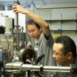 Two men work on scientific equipment in a laboratory.