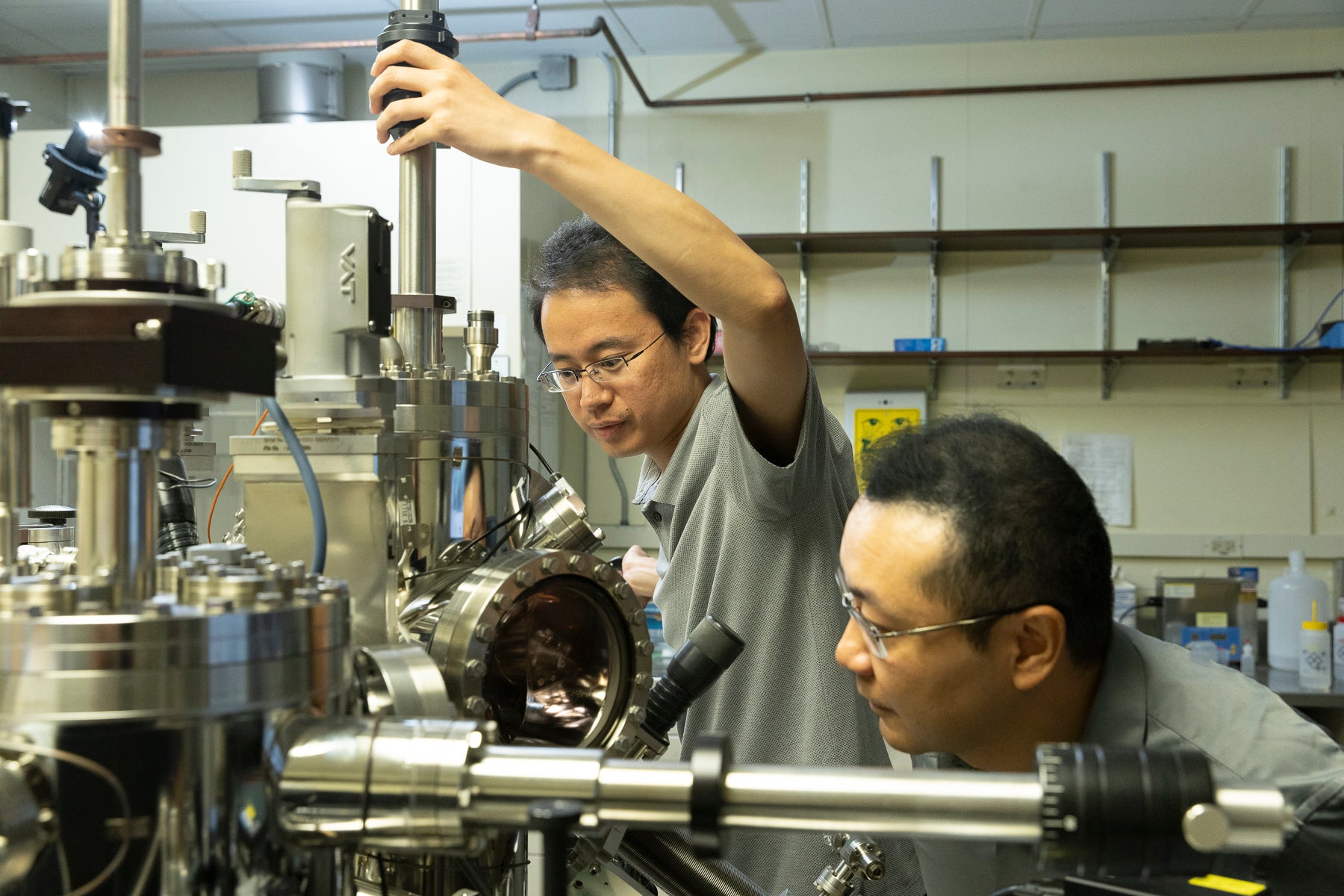 Two men work on scientific equipment in a laboratory.