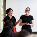 two women stand in front of an audience to accept an award.