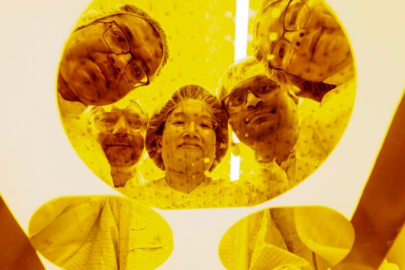 Five people in hair caps and gowns look down at the camera through a circular lens with a yellow tint.