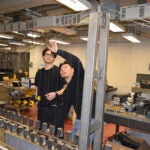 two men work on a model of a bridge in a lab