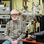 A man wearing safety glasses sits among equipment in a lab