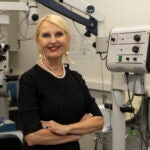 A woman in a black dress poses next to medical equipment in a lab