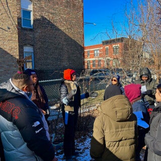 UIC students volunteered at the East Garfield Park garden of Limes Smiles for Miles for the 2025 MLK Jr. Day of Service. They helped winterize the garden, picked up trash and planted native flowers. (Photo: Parrama Chouhan) a woman talks with volunteers outside at a garden in winter